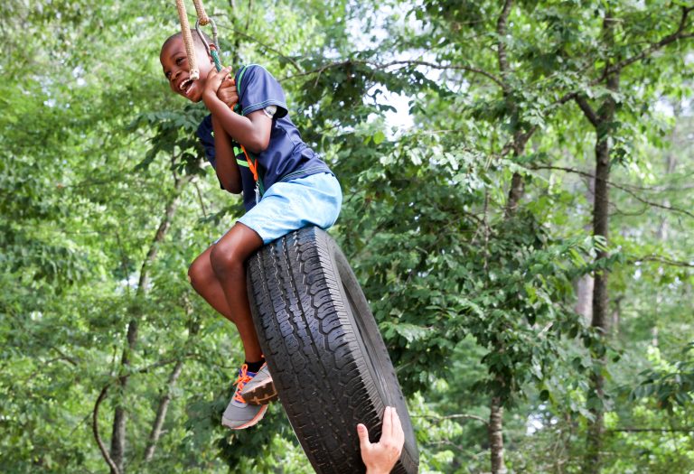 A young boy smiles as he is pushed on a tire swing.