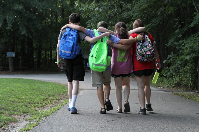 Four campers walk away from the camera, their arms around each others' shoulders.