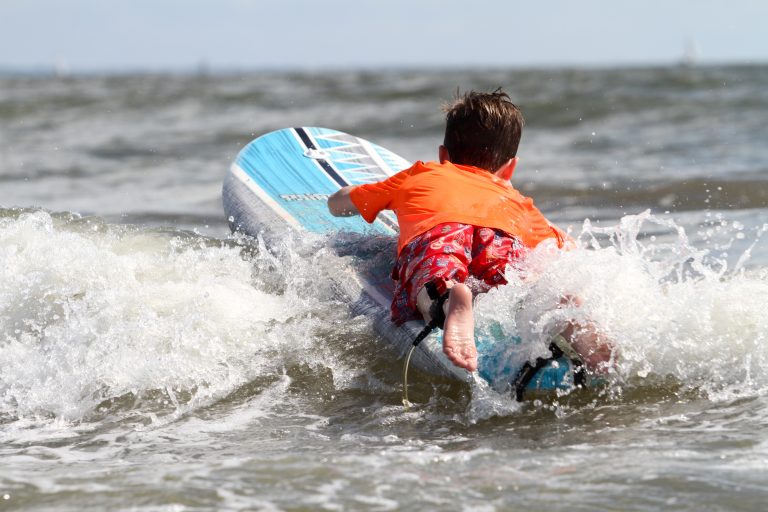 A boy tackles a wave while riding prone on a surfboard.
