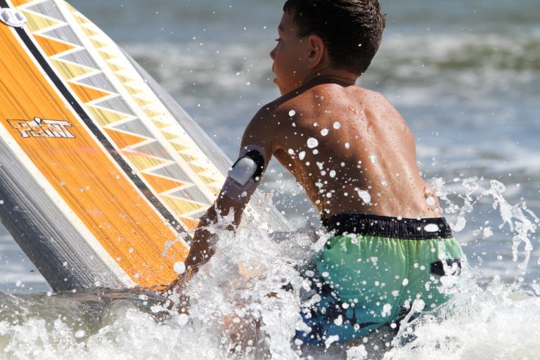 A boy tackles a wave while kneeling on a surfboard.